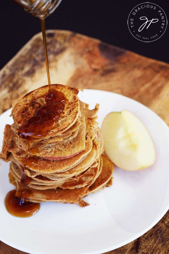 Maple syrup being poured over a tall stack of Healthy Apple Ring Pancakes.