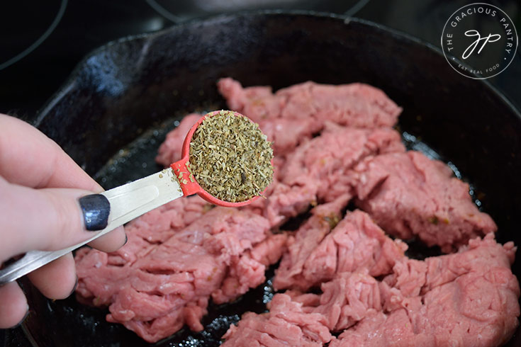Adding Italian seasoning to ground meat in a skillet.