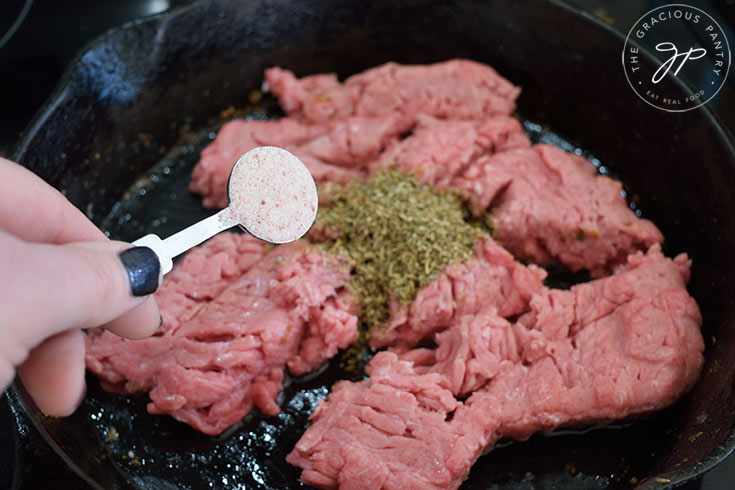 Adding salt to ground meat in a skillet.