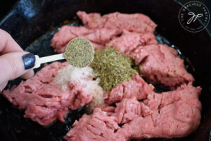 Adding pepper to ground meat in a skillet.