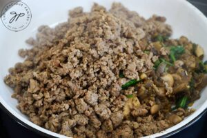 Cooked ground turkey set aside atop a plate holding sautéd vegetables.