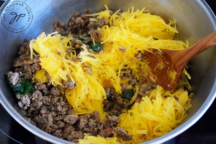 Spaghetti squash "spaghetti", ground turkey, and sautéd vegetables sitting in a mixing bowl with a wooden spoon.