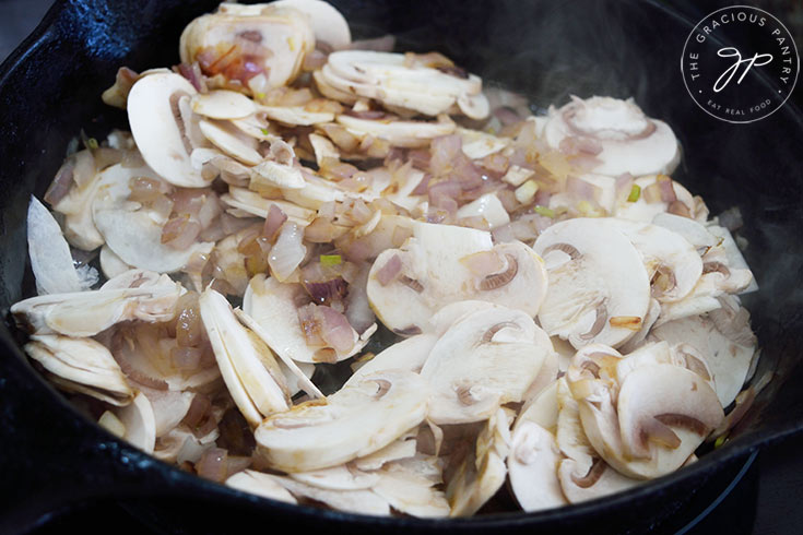 Mushroom slices added to onions in a cast iron skillet.