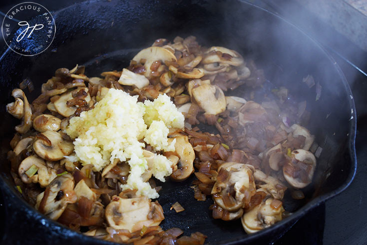 Pressed garlic added to onions and mushrooms in a cast iron skillet.