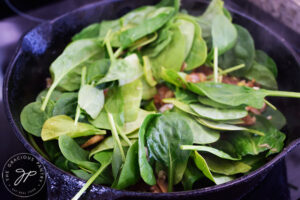 Raw baby spinach leaves added to mushrooms, onions and garlic in a cast iron skillet.