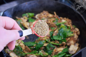 Adding Italian seasoning to sautéd vegetables in a cast iron skillet.