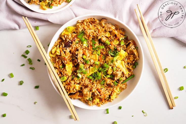 The finished Healthy Pork Fried Rice served in a white bowl with some chop sticks resting on the side of the bowl.