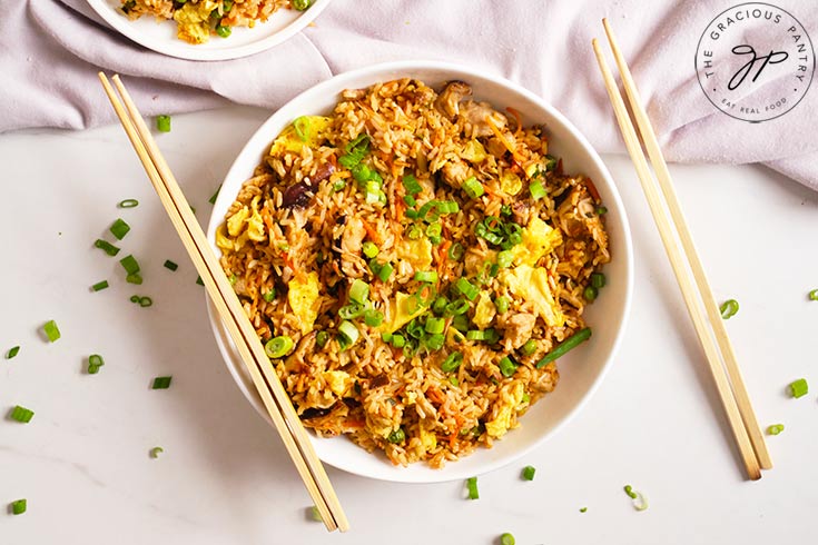 The finished Healthy Pork Fried Rice served in a white bowl with some chop sticks resting on the side of the bowl.