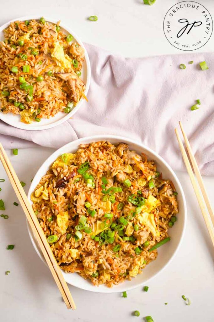 Two plates hold servings of Healthy Pork Fried Rice. Chopsticks rest to the sides of the dishes.