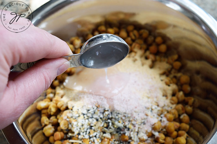 Adding oil to a bowl or roasted chickpeas and spices.