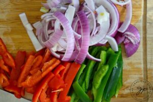 Red and green bell peppers and a purple onion sliced into long slices for this Sheet Pan Shrimp Fajitas Recipe.