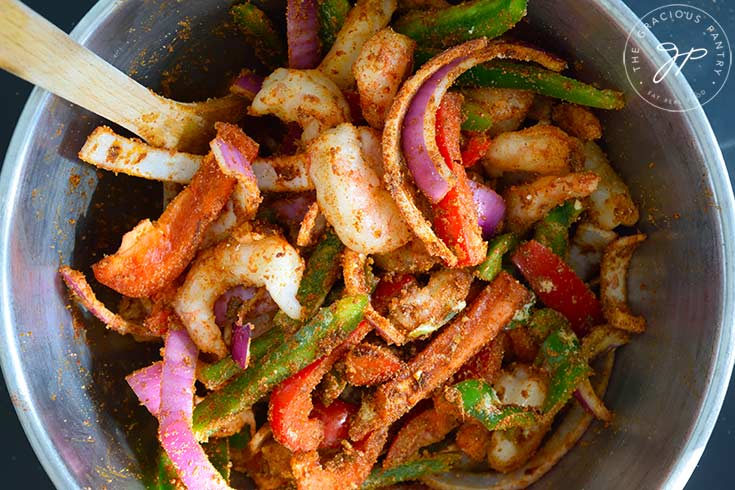 Sheet Pan Shrimp Fajitas Recipe ingredients mixed together with spices and oil in a large mixing bowl.