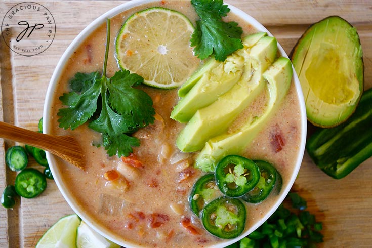 A white bowl filled with Crockpot White Chicken Chili is garnished with lime, cilantro, avocado and jalapeno peppers.
