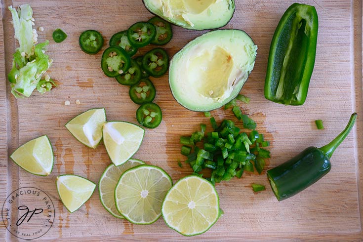 Prepped garnishes laying on a wood cutting board. Chunks and slices of lime, jalapeno pepper and avocado.