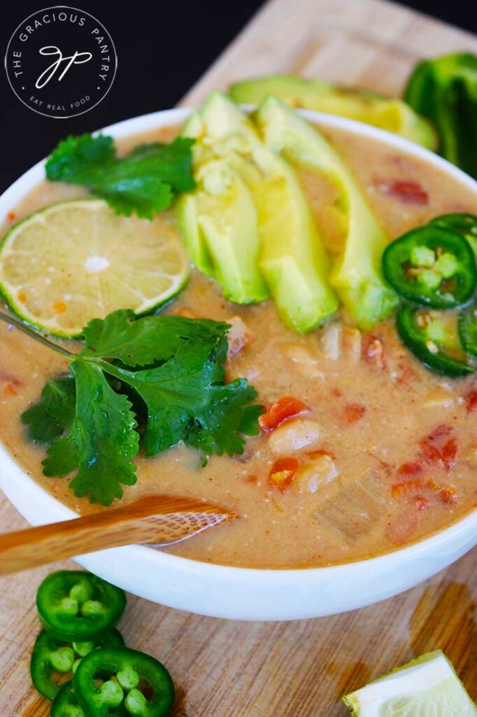 A close up of a bowl of Crockpot White Chicken Chili garnished with lime, cilantro, avocado slices and jalapeno pepper slices.