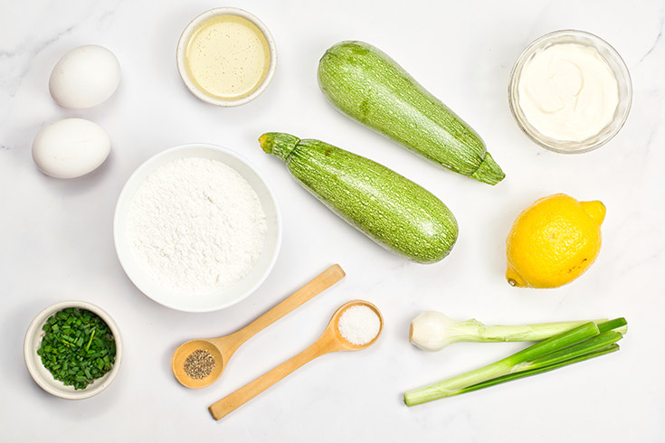 All the ingredients for this Zucchini Fritters Recipe gathered together on a white surface.