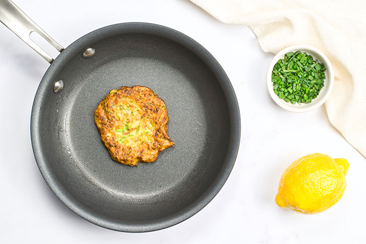 A cooked zucchini fritter sits in an pan, just cooked.