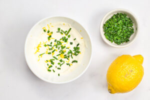 Yogurt in a small white bowl mixed with fresh lemon zest and chives.