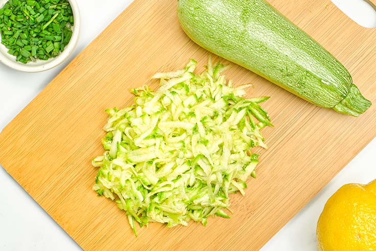 Grated zucchin sitting on a cutting board next to a whole zucchini.