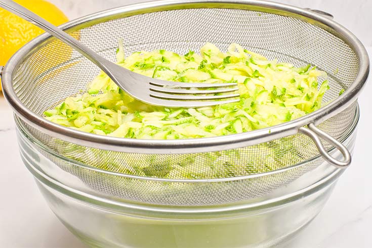 Grated zucchini in a mesh sieve being pressed to remove water.