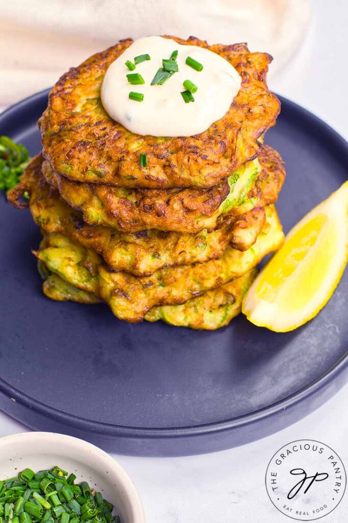 And angled view looking at a stack of Zucchini Fritters on a plate with a single lemon wedge.