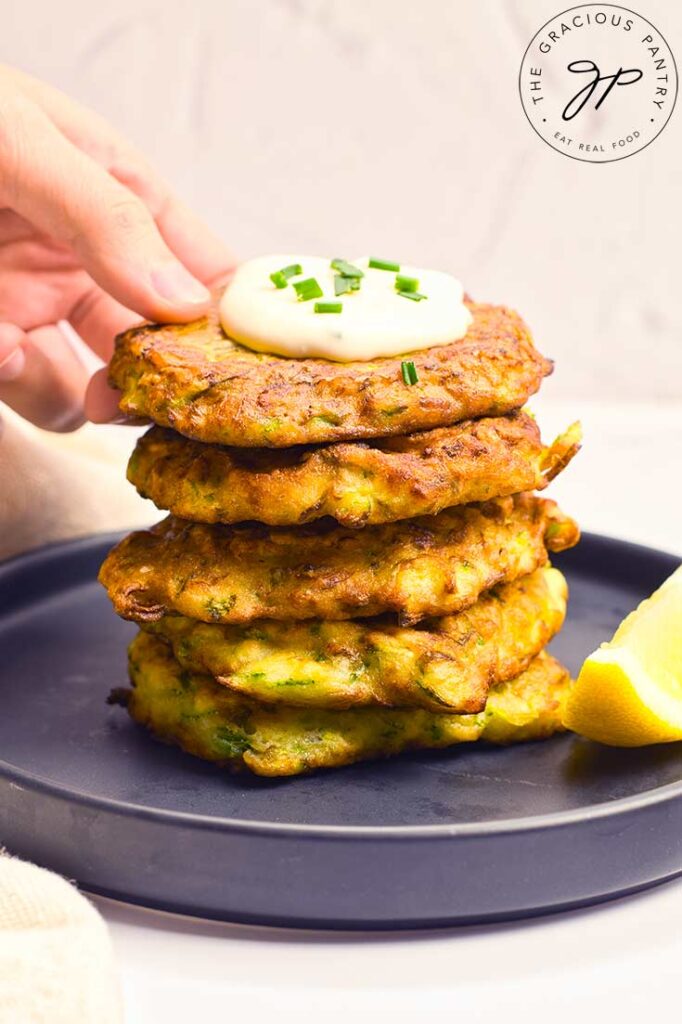 A female hand reaches for the top Zucchini Fritter from a stack of them on a plate.