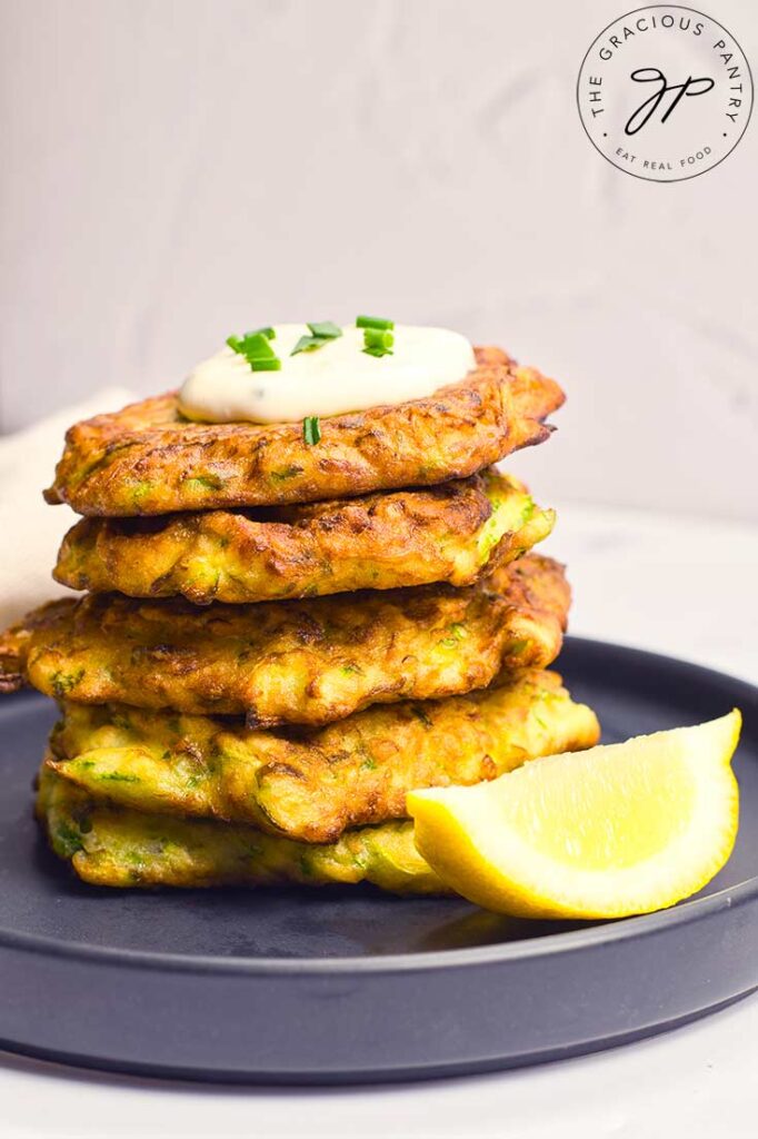 A tall stack of Zucchini Fritters sit on a gray plate with a wedge of lemmon.