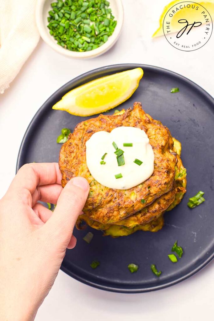 An overhead view of a female hand reaching for the top zucchini fritter from a stack of them on a plate.