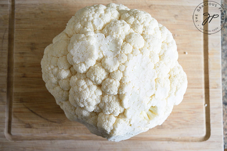 A cleaned head of cauliflower sitting on a cutting board.