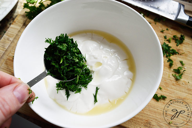 Adding fresh, chopped parsley to yogurt in a mixing bowl.