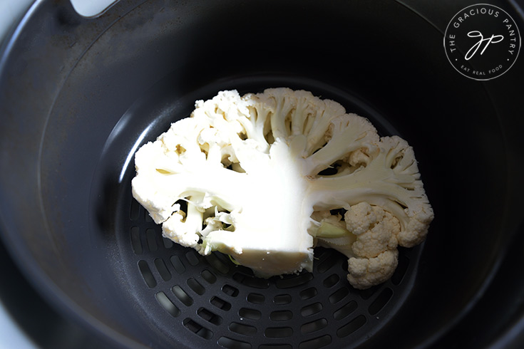 A single cauliflower steak sitting in an air fryer basket.
