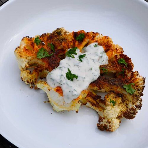 A front view of a single Air Fryer Cauliflower Steak with yogurt sauce on top.