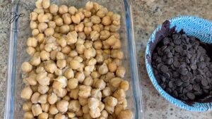 Cooked beans in a glass dish with a bowl of chocolate chips next to it.