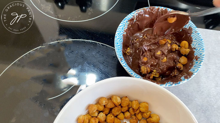 Roasted chickpeas being stirred into melted chocolate.