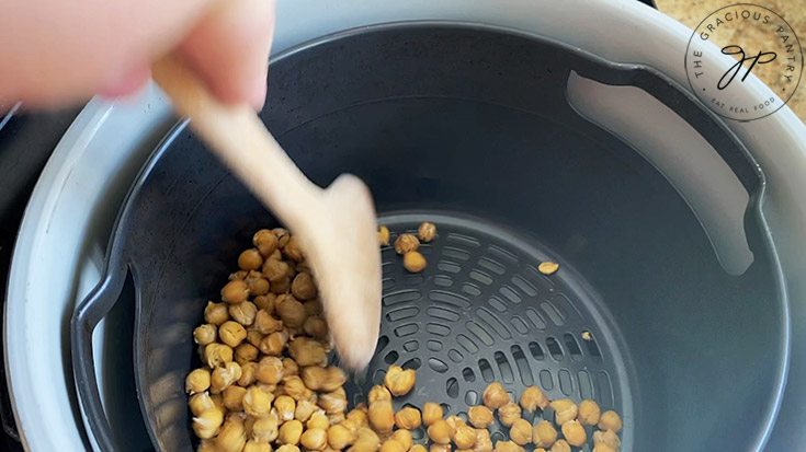Stirring chickpeas in an air fryer basket.