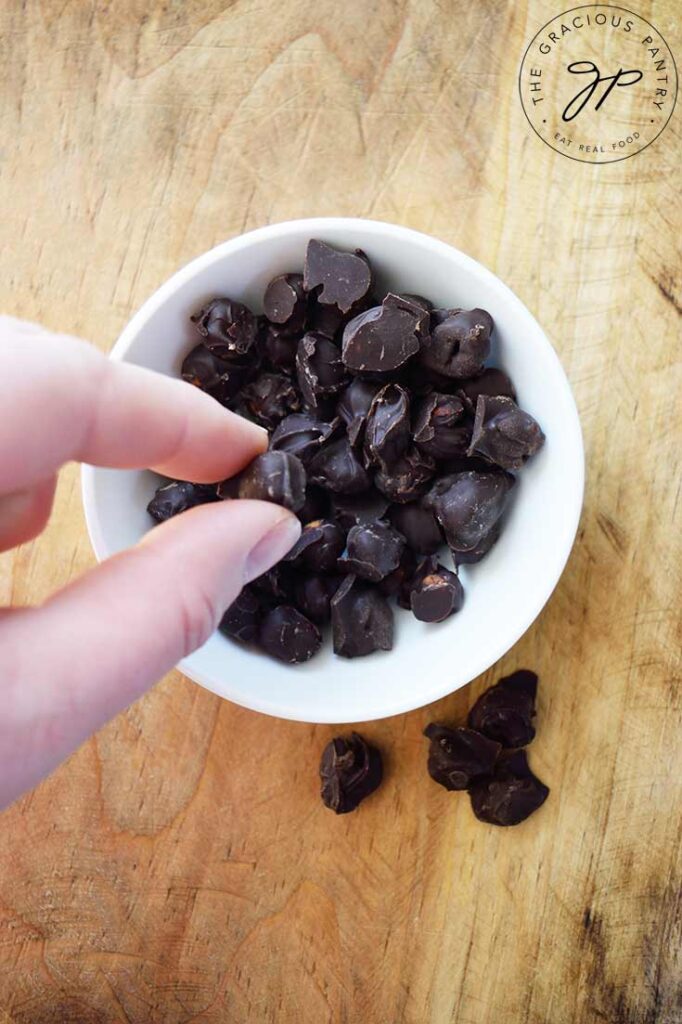A hand picks up a single Chocolate Covered Chickpea from a bowl filled with them.