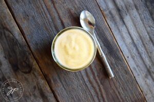 And overhead view of a small glass jar filled with Pumpkin Spice Yogurt. A stainless steel spoon lays to the right of the jar on a wood surface.