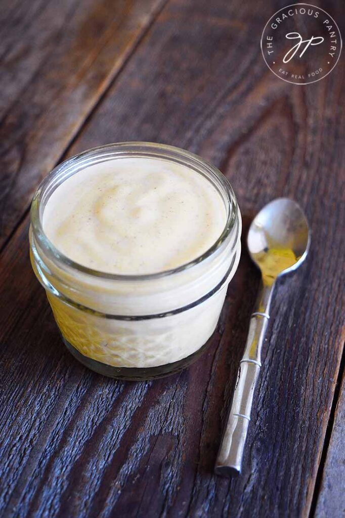 A side view of a small, glass jar filled with Pumpkin Spice Yogurt. A spoon rests to the right of the jar.