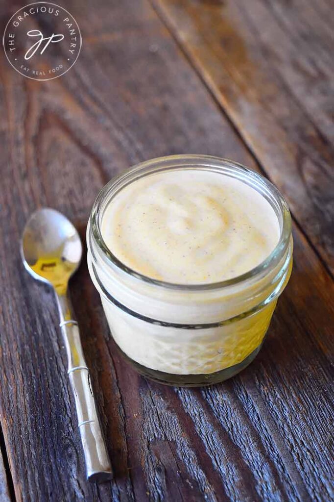 A front view of a small, glass jar filled with Pumpkin Spice Yogurt. A spoon rests to the left of the jar.