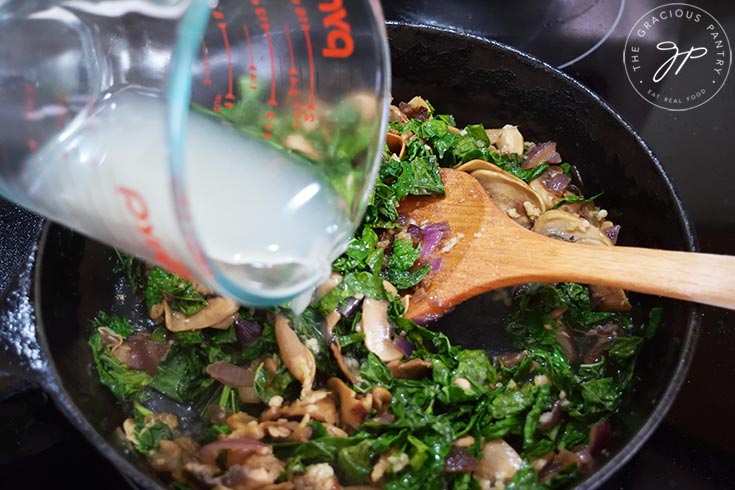 Pouring broth into a pan of sautéing vegetables.