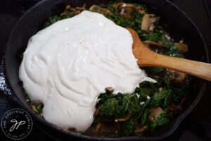 Yogurt added to a pan of sautéing vegetables in a skillet.
