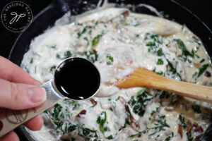 Adding balsamic vinegar to the Creamy Kale And Mushroom Pasta sauce in a cast iron skillet.