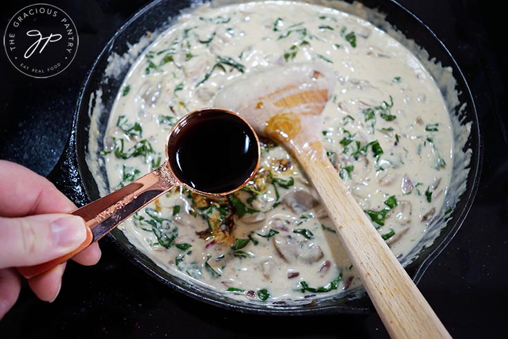 Adding soy sauce to Creamy Kale And Mushroom Pasta sauce in a cast iron skillet.