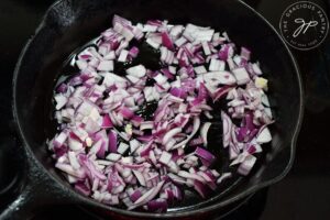 Chopped, red onions sautéing in a cast iron skillet.