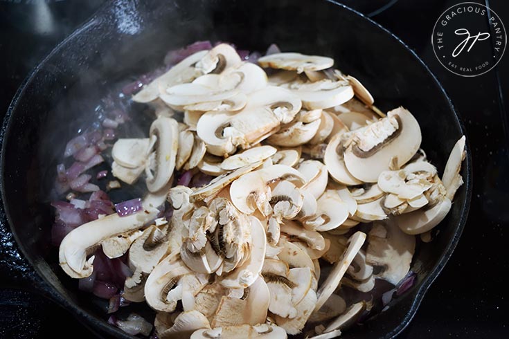 Mushrooms added to onions in a cast iron skillet.