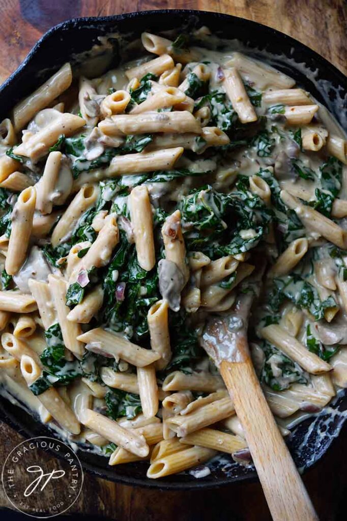 An overhead view looking down into a cast iron skillet filled with Creamy Kale And Mushroom Pasta.