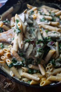A wooden spoon lifts some Creamy Kale And Mushroom Pasta out of a skillet.