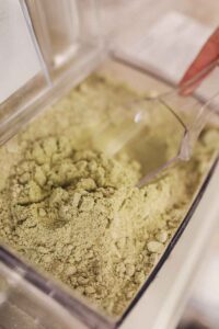 A plastic scoop sitting in a plastic bin of green-ish protein powder.