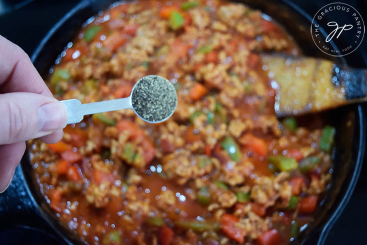 Adding pepper to a skillet full of Healthy Turkey Sloppy Joes filling.