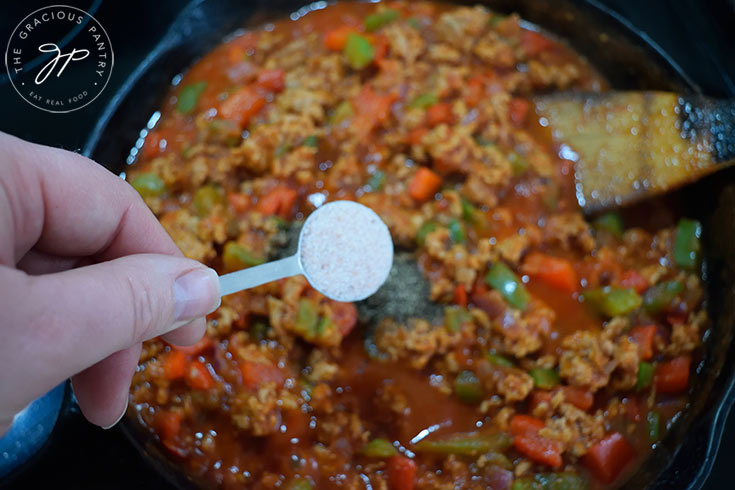 Adding salt to a skillet full of Healthy Turkey Sloppy Joes filling.